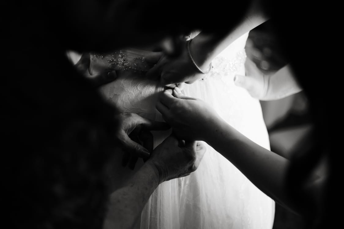 Black and white image of wedding dress getting buttoned up