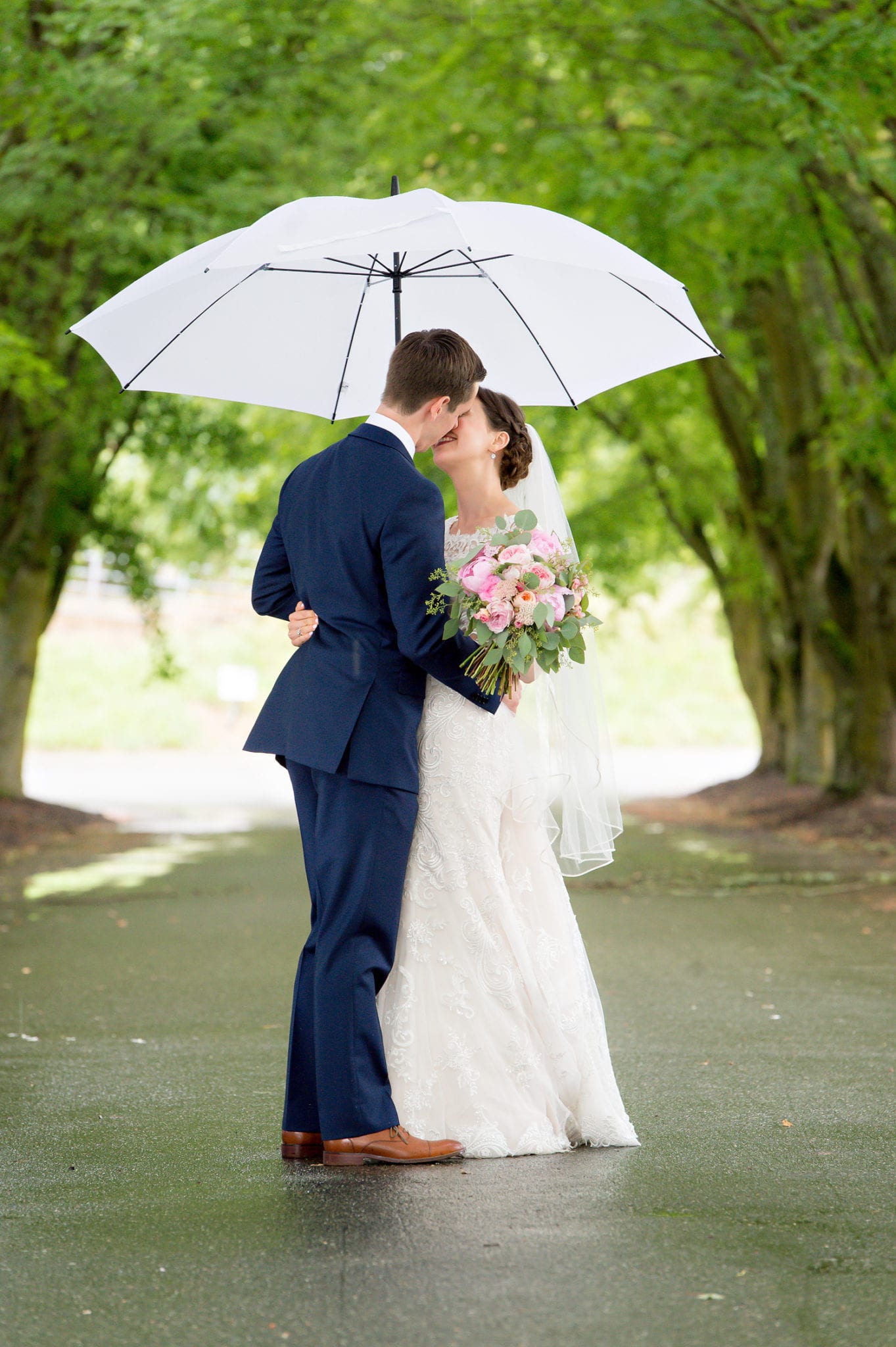 Bride and groom portrait with an umbrella in the row of trees at Maplehurst Farm wedding venue