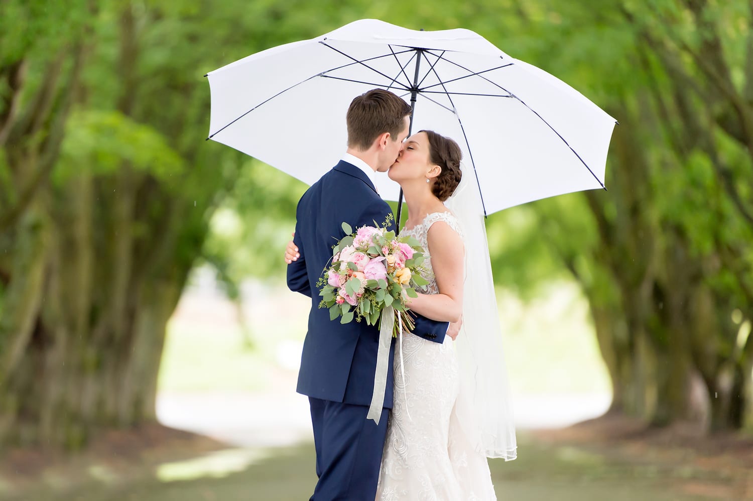 Bride and groom kissing in the rain with an umbrella at Maplehurst Farm wedding venue